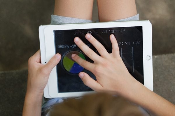 A child outside holding a tablet with an overlay. They are exploring the overlay with their finger.