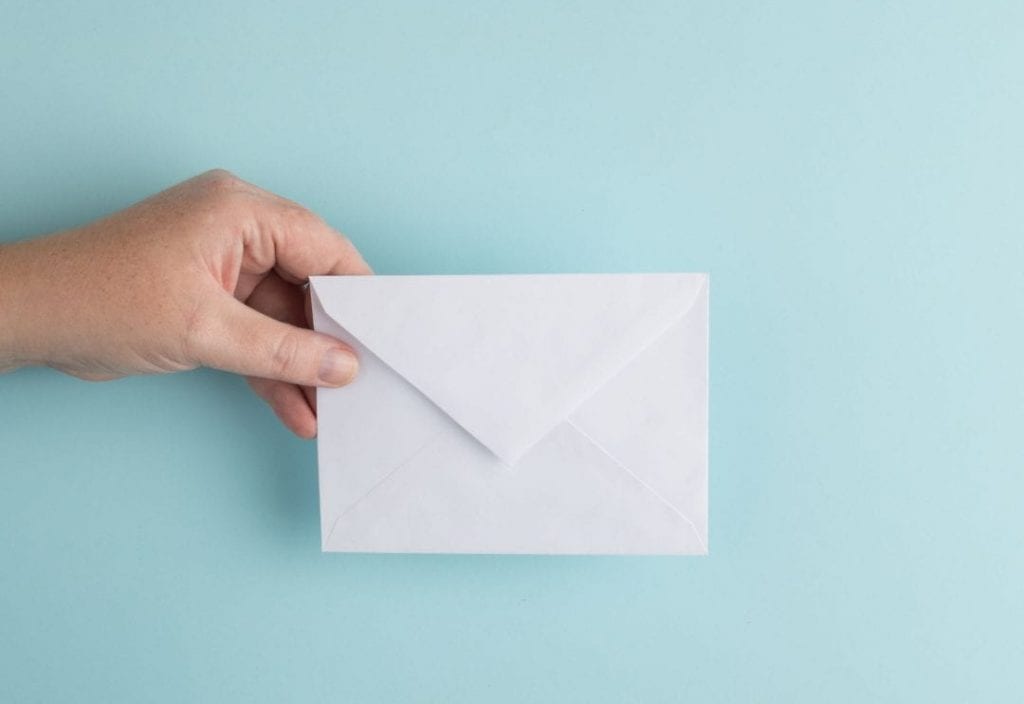 a hand holding a white envelope on a light blue background