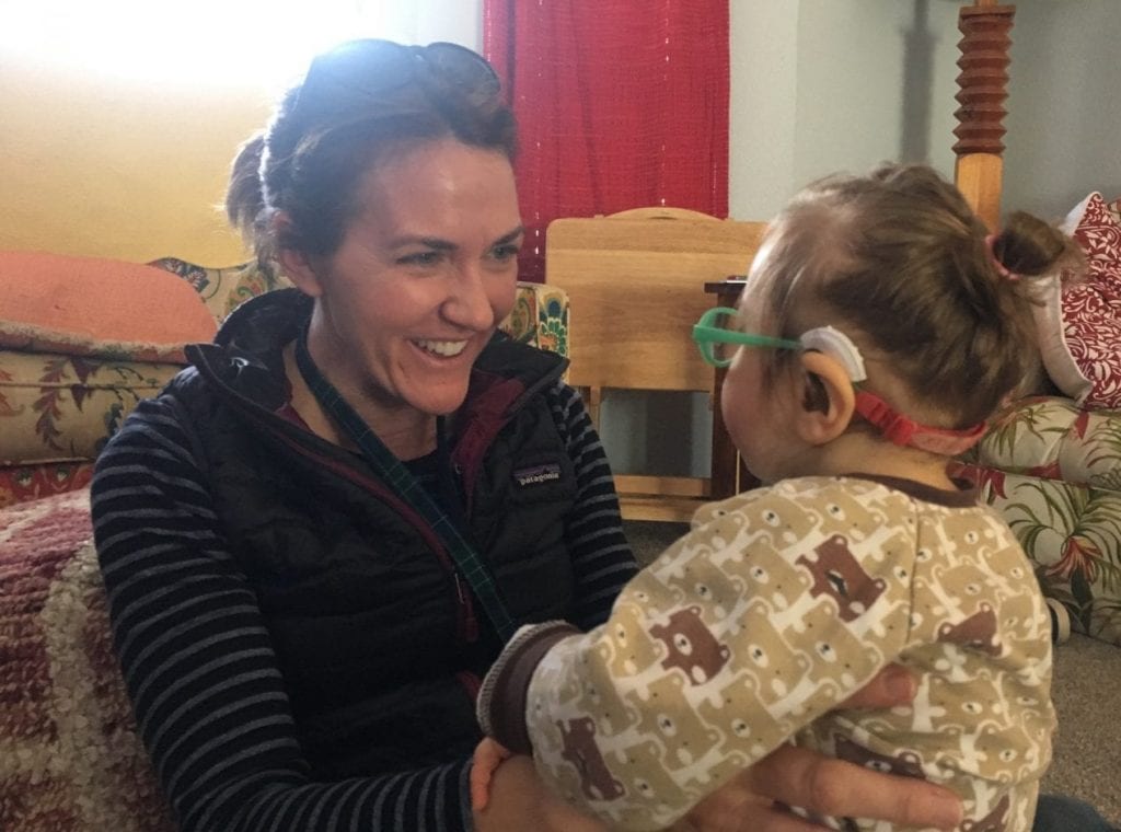 Andrea working with a young student wearing glasses and a hearing aid in a home setting