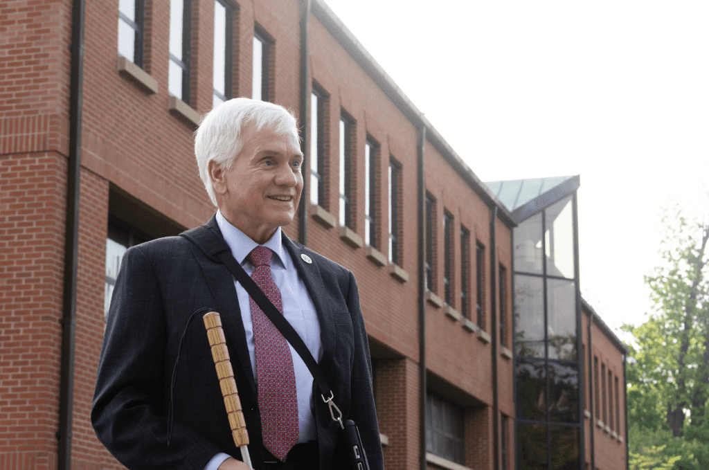 Gary Mudd standing outside a building in a suit carrying a white cane