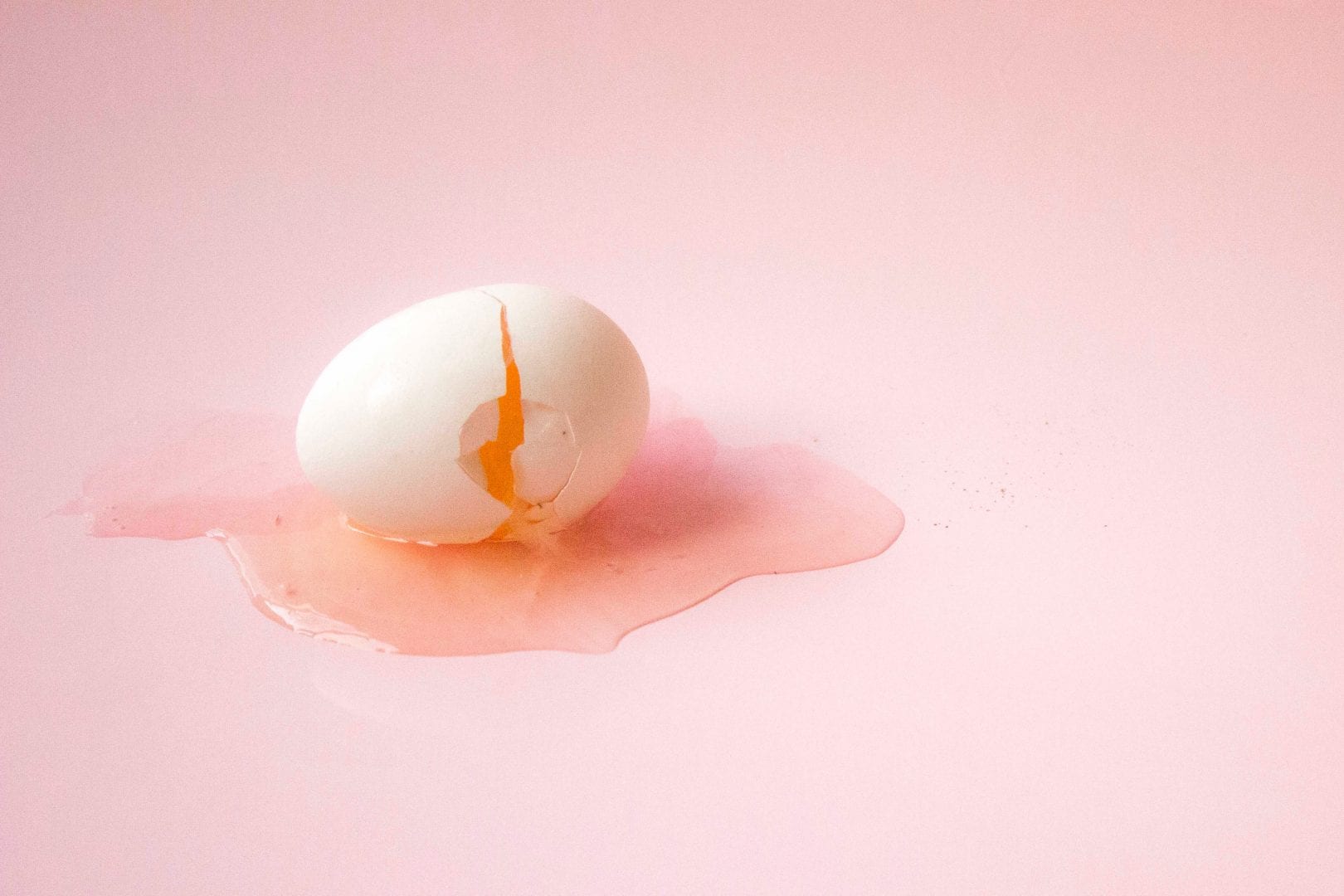 a cracked egg on a pale pink background