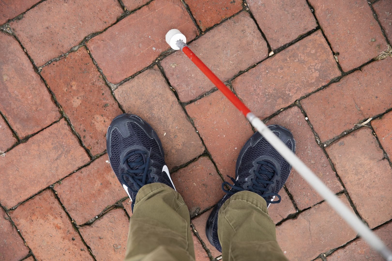 birds eye view of sneakered feet and a white cane on brick