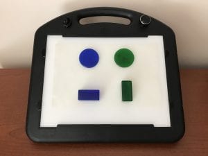 A blue circle and a green circle appear to float over a blue block and a green block respectively. All pieces are attached to the LED Mini-Lite Box surface with a sheet of Dycem