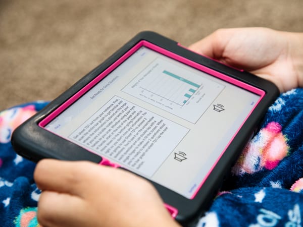 a child holding a tablet showing a paragraph of information and a bar chart