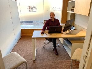 Lee Huffman smiling and sitting in a clean and bright office back lit by a frosted window