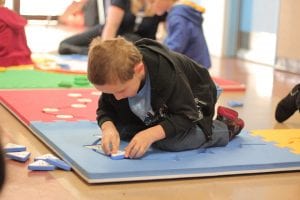 At the Guide Dogs Victoria camp, a young boy with low vision is having fun playing a Reach & Match game with their peers.