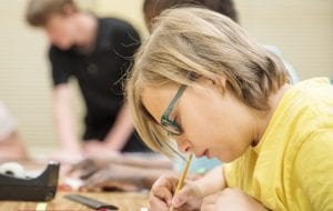 a student in glasses working at a desk with a pencil