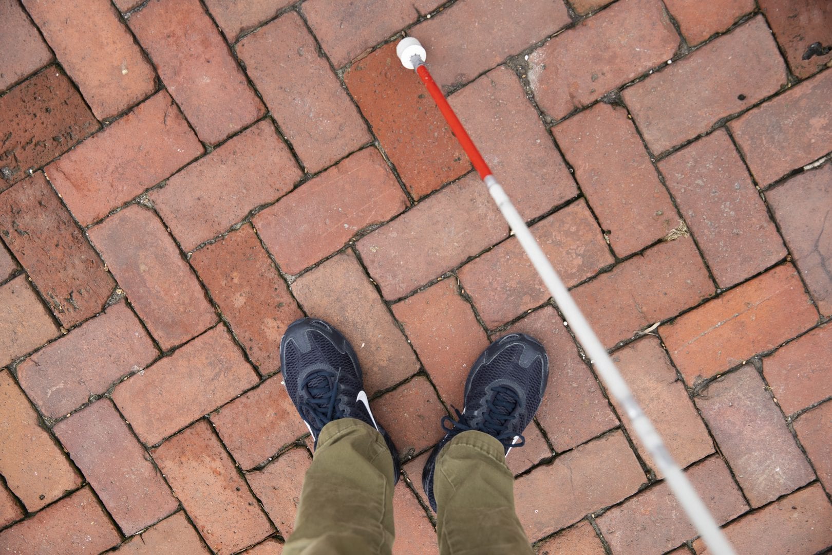 birds eye view of someone standing on a brick path with a white cane