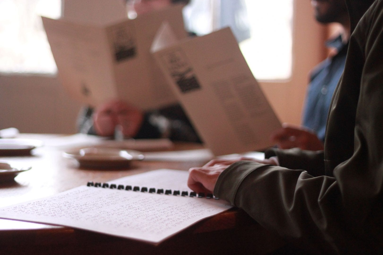 A close up on the hands of someone seated in a restaurant reading a braille menu