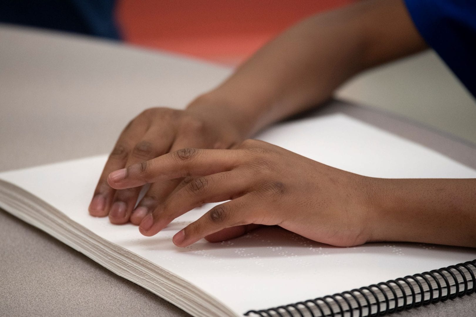 A close up of the hands of someone reading spiral bound braille
