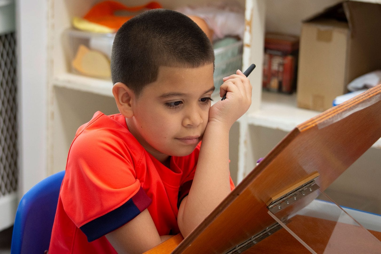 A student seated at a table working from a book stand