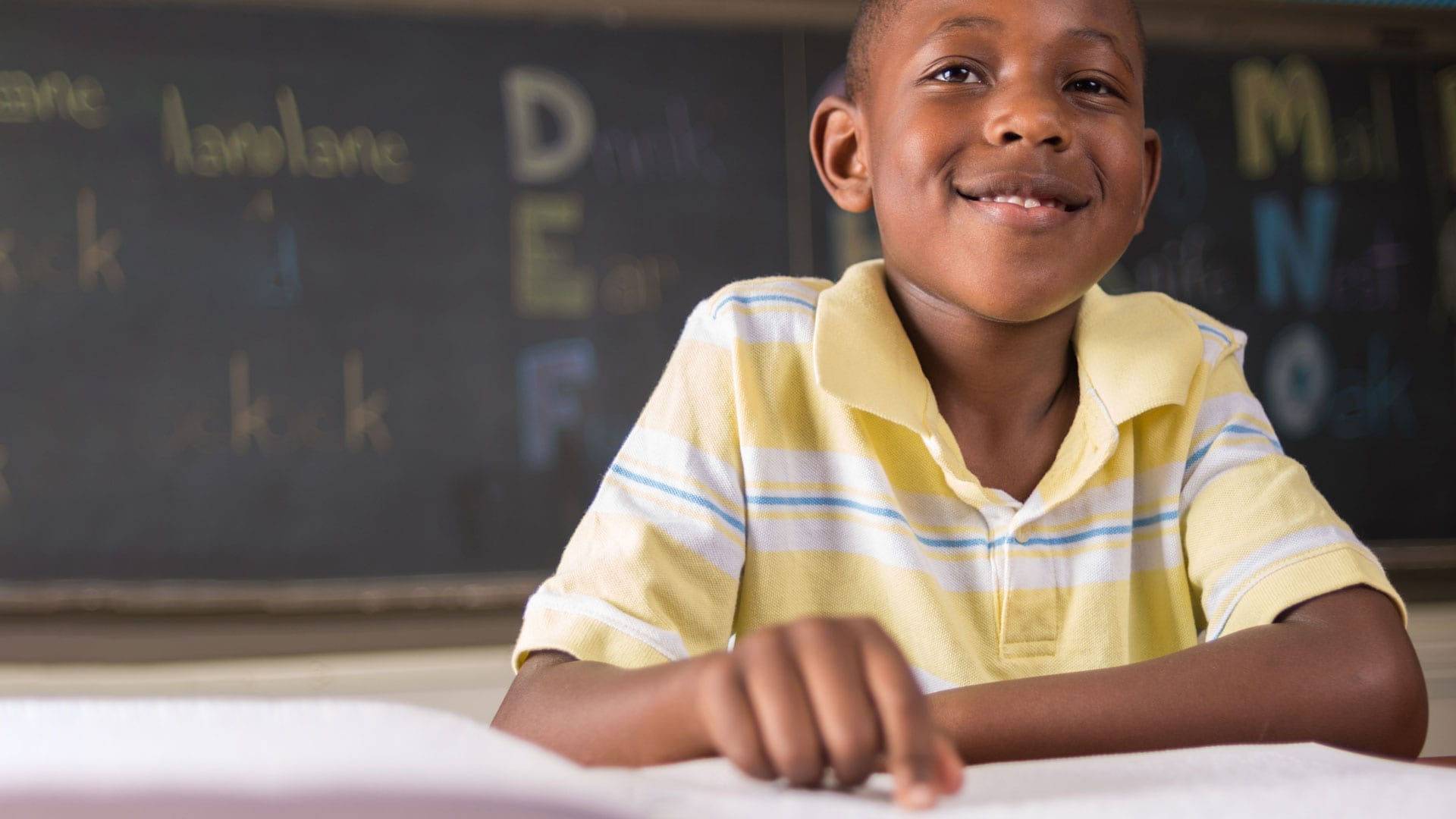 A smiling boy with his hand on an open book.