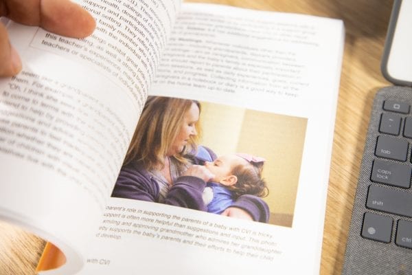 The Babies with CVI book is held open to a page that includes an image of a woman and infant.