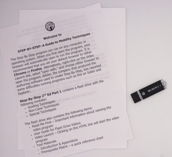 A copy of the Step-by-Step user guide printed on white paper laid on a white surface next to the black Step-by-Step Part 1 USB thumb drive.