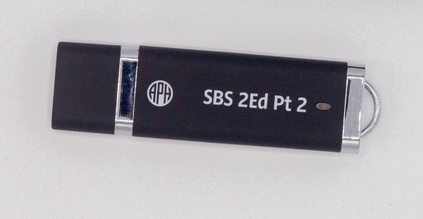 Close-up of the black Step-by-Step Part 2 thumb drive against a white background. In white lettering, it says "SBS 2Ed Pt 2.