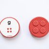 The front and back of a red, circular Reach & Match Alphabet Tile showing the letter g in print and braille.