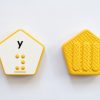 The front and back of a yellow, hexagonal Reach & Match Alphabet Tile showing the letter y in print and braille.