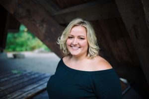 a portrait style photo of Stacey smiling in a black blouse in front of an old wooden structure