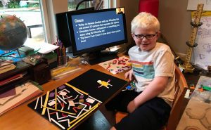 a student smiling in front of a computer with a presentation on the screen. the Picture Maker Wheatley Tactile Diagramming Kit sits on the table next to them showing extra pieces to the left and the figure of a person on the right.