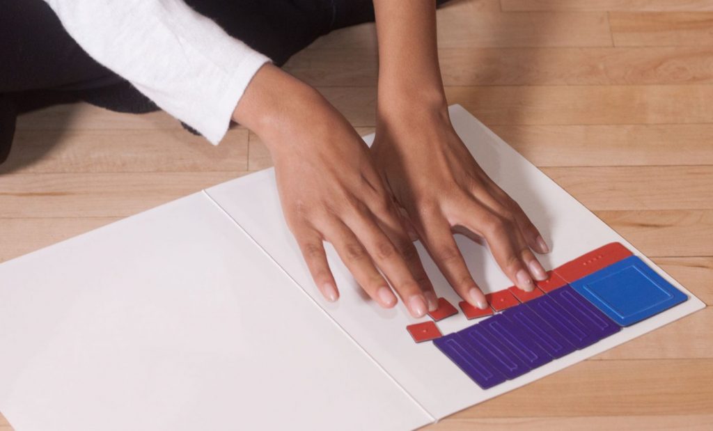 students hands counting by arranging tiles of different colors, textures, and sizes on a white background