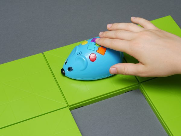 A child's hand moves the blue Code and Go Mouse along a row of lime green squares.