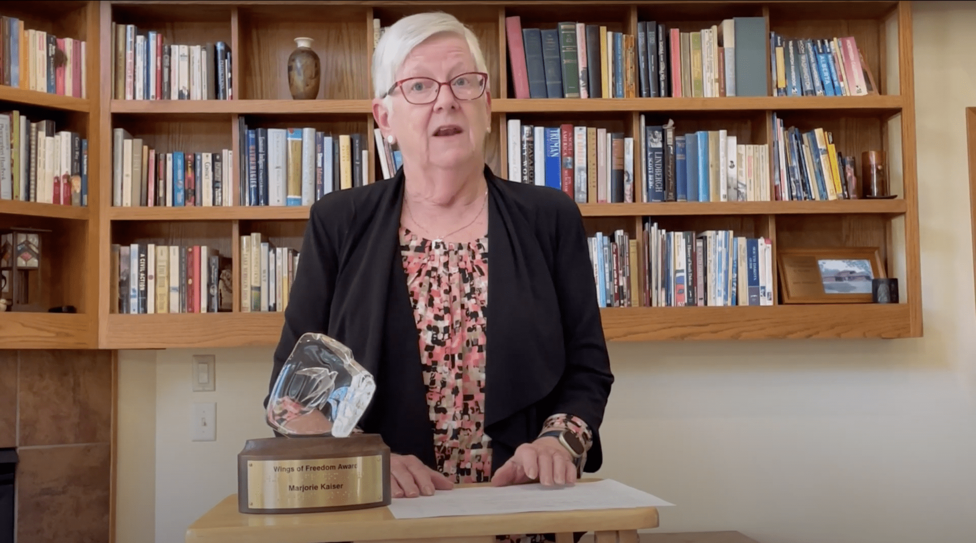 Marje Kaiser standing at a podium with wings of freedom award next to her