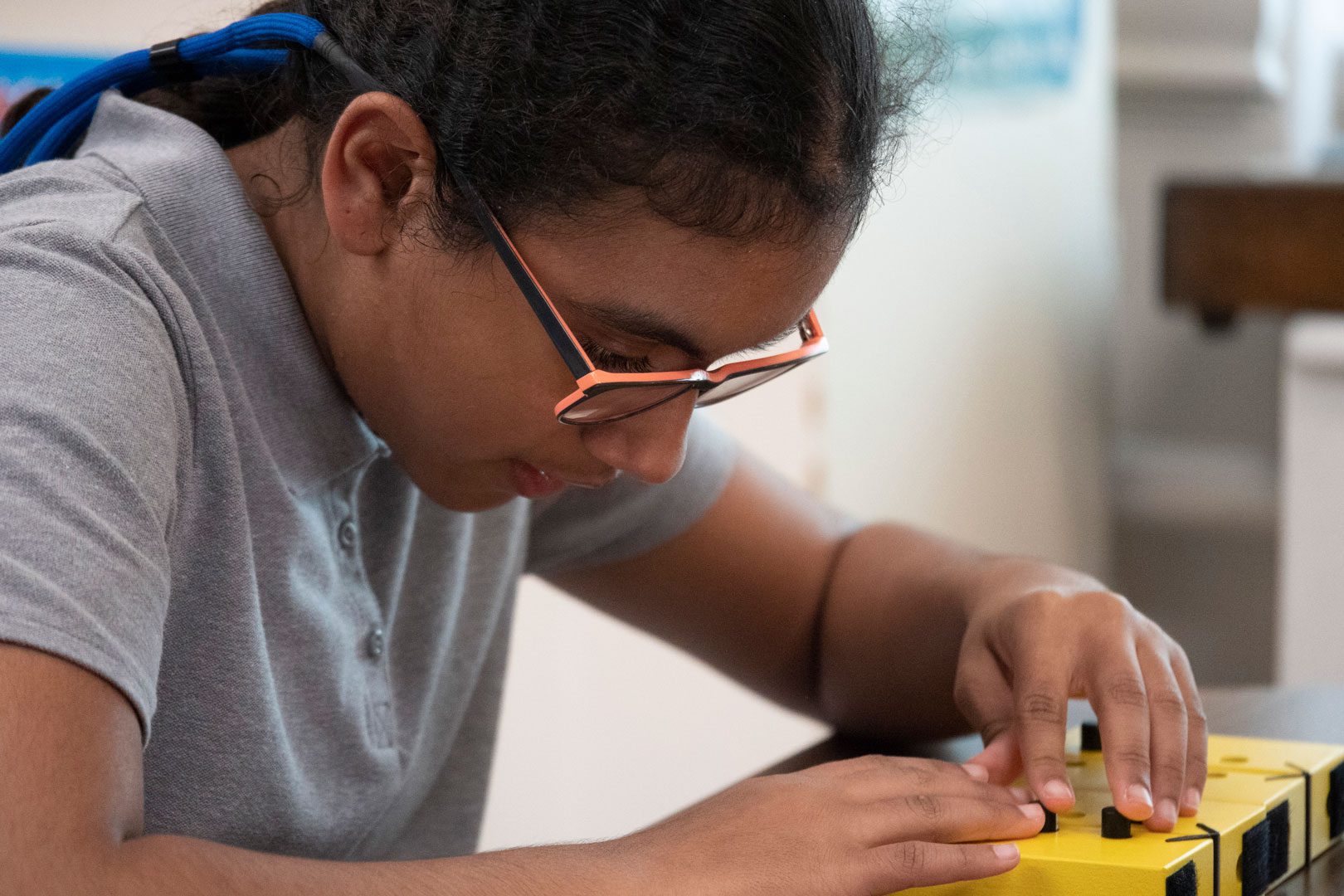 A young student wearing glasses and sitting at a table exploring a braille learning manipulative.