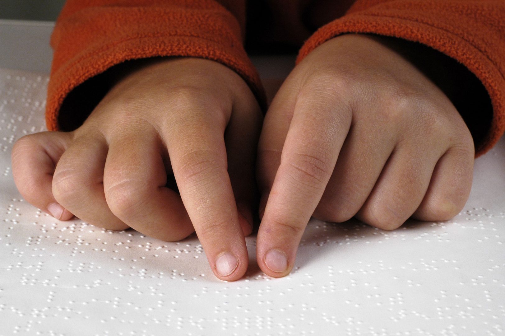 A child's hands with index fingers extended on a braille page.