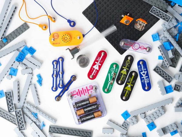 An array of BRIC: Structures kit components strewed out on a white surface. Pictured are building blocks, a base plate, several switches and other electrical components, snaps, and a variety of cables.