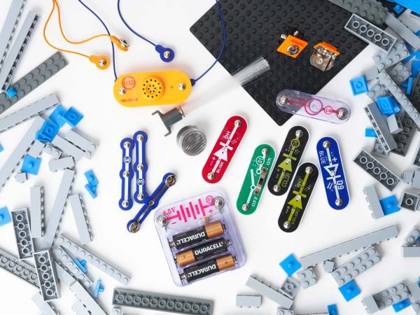 An array of BRIC: Structures kit components strewed out on a white surface. Pictured are building blocks, a base plate, several switches and other electrical components, snaps, and a variety of cables.