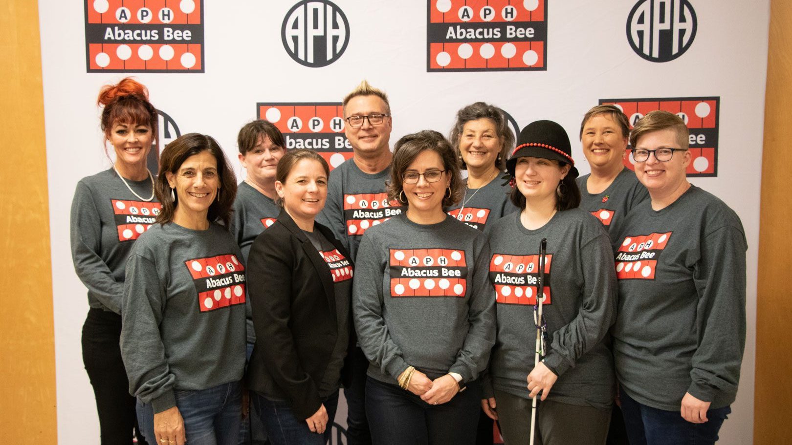 10 members of the Outreach team posed together smiling. They are all wearing APH Abacus Bee logoed shirts.