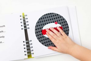 A child’s hand touching the monster’s red textured mouth and raised pointy teeth.