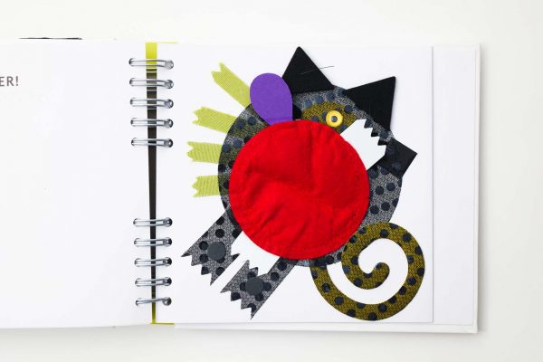 The abstract monster and all of his bizarre physical traits made of various textures including the small black dot textured pattern, the long curling tail, fuzzy felt ears, and a plastic eye.