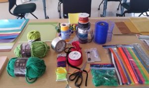 A table full of art supplies including pipe cleaners, pompoms, yarn, ribbon, tape, scissors, and paper. 