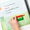 A child uses their hand to move the orange caterpillar across a patch of tall, green grass with the text and braille on the page reading, “A caterpillar in my backyard. He is small, SOFT, and a little bit prickly.”
