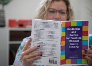 A seated woman reading a copy of Guidelines and Games for Teaching Efficient Braille Reading.