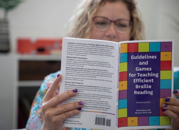 A seated woman reading a copy of Guidelines and Games for Teaching Efficient Braille Reading.