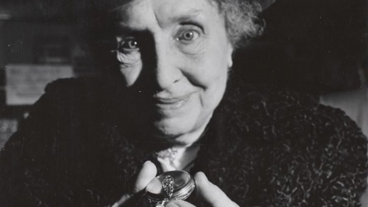Close up of Helen Keller’s face as she smiles and holds up a pocket watch.