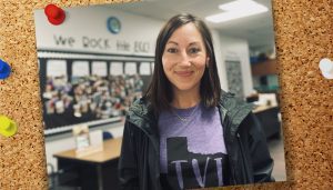 A photo of Stacey smiling and standing in her colorfully decorated classroom pinned on a bulletin board.