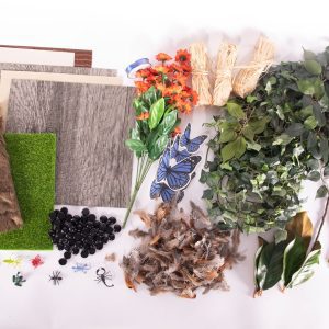 Shows an array of the items included in the Tactile Theme Pack: In My Yard, including small and large artificial leaves and flowers, an artificial turf mat, fake fur, flat-backed pebbles, plastic insects, rubber earthworms, bird feathers, plastic butterflies, raffia, blue satin ribbon, and textured sheets (bark, reptile, lizard skin, fuzzy).