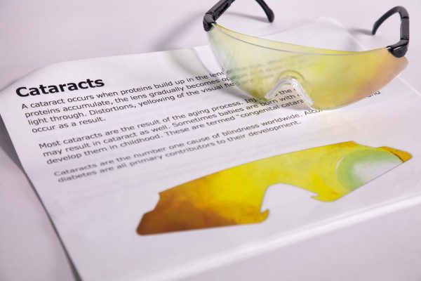 A pair of safety glasses containing the Cataracts insert sits on top of a printed page with information about the condition and an image of the insert laid flat.