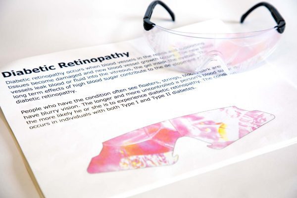 A pair of safety glasses containing the Diabetic Retinopathy insert sits on top of a printed page with information about the condition and an image of the insert laid flat