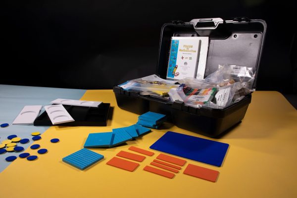 Front view of FOCUS in Mathematics kit opened up to show organized manipulatives, some of the items are spread out on the table the kit is resting on.