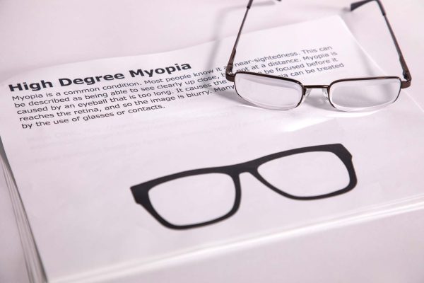 A pair of safety glasses containing the Myopia insert sits on top of a printed page with information about the condition and an image of the insert laid flat