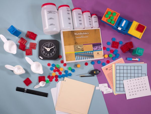 Bird's eye view of MathBuilders Unit 5 Kit: Measurements and Estimation spread out to show the kits’ components including an analog clock, clock face sheets, metric-English measurement ruler, a guidebook, and more.