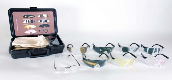 All eight pairs of glasses included in the kit that mimic common eye conditions are laid out against a white background. To the left of the glasses is the box they come in with a visual guide to identify which inserts represent which conditions.