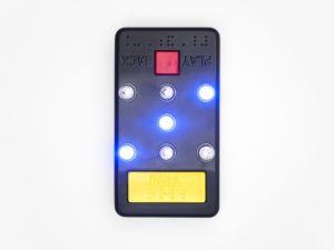Talking Glow Dice displaying three lit dots. The device is black with a square red button at the top and a rectangular yellow button at the bottom.