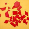 Red tactile manipulatives resting on a yellow background. The red manipulatives include rhombuses, triangles, squares, rectangles, and a hexagon.