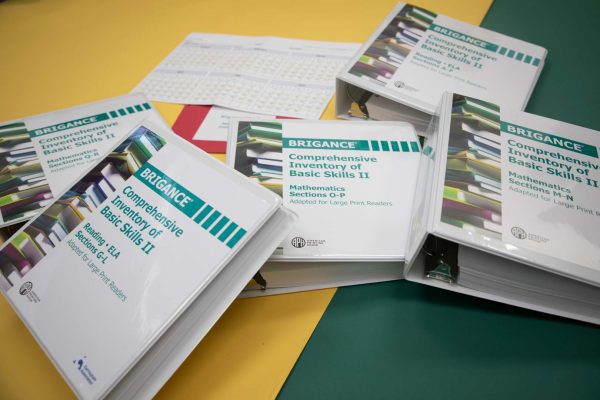 Large print Brigance binders loosely stacked on top of one another. The binders are resting on a yellow and green surface.