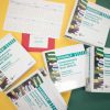 Five large print Brigance assessment binders, red mathematics foldout pages, and a calendar showing January through June rest on top of a yellow and green surface.